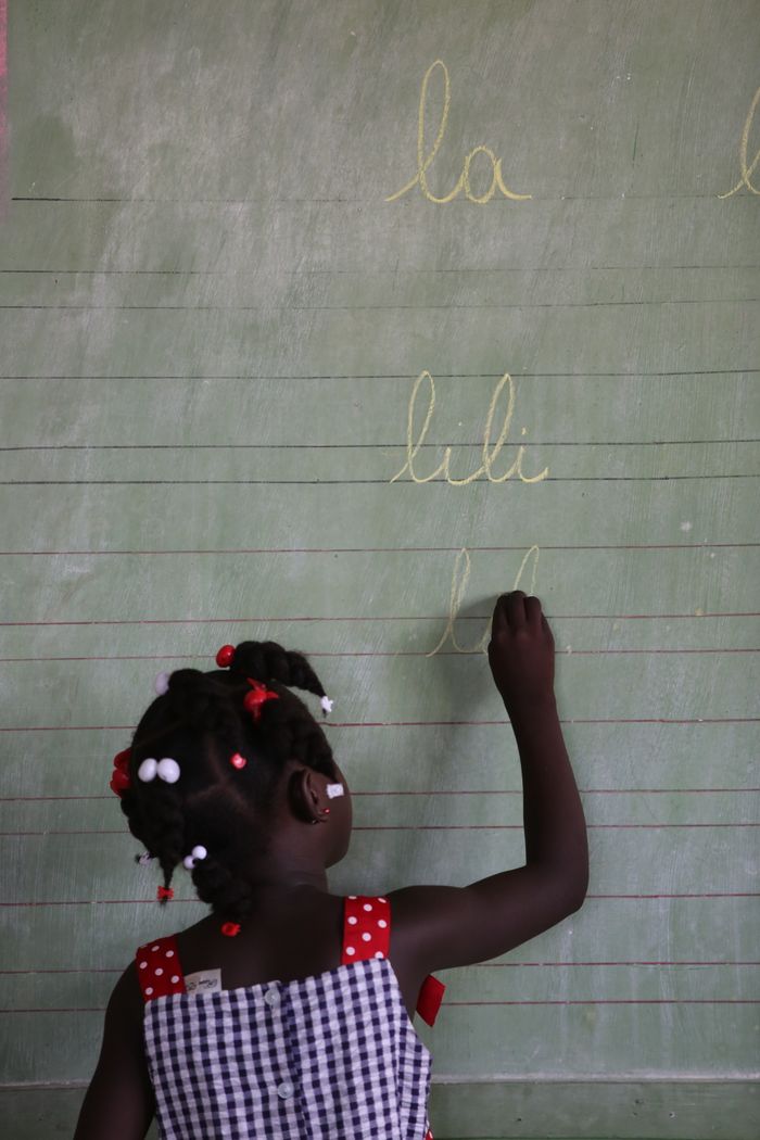 Young girl writing on green blackboard in a classroom setting.