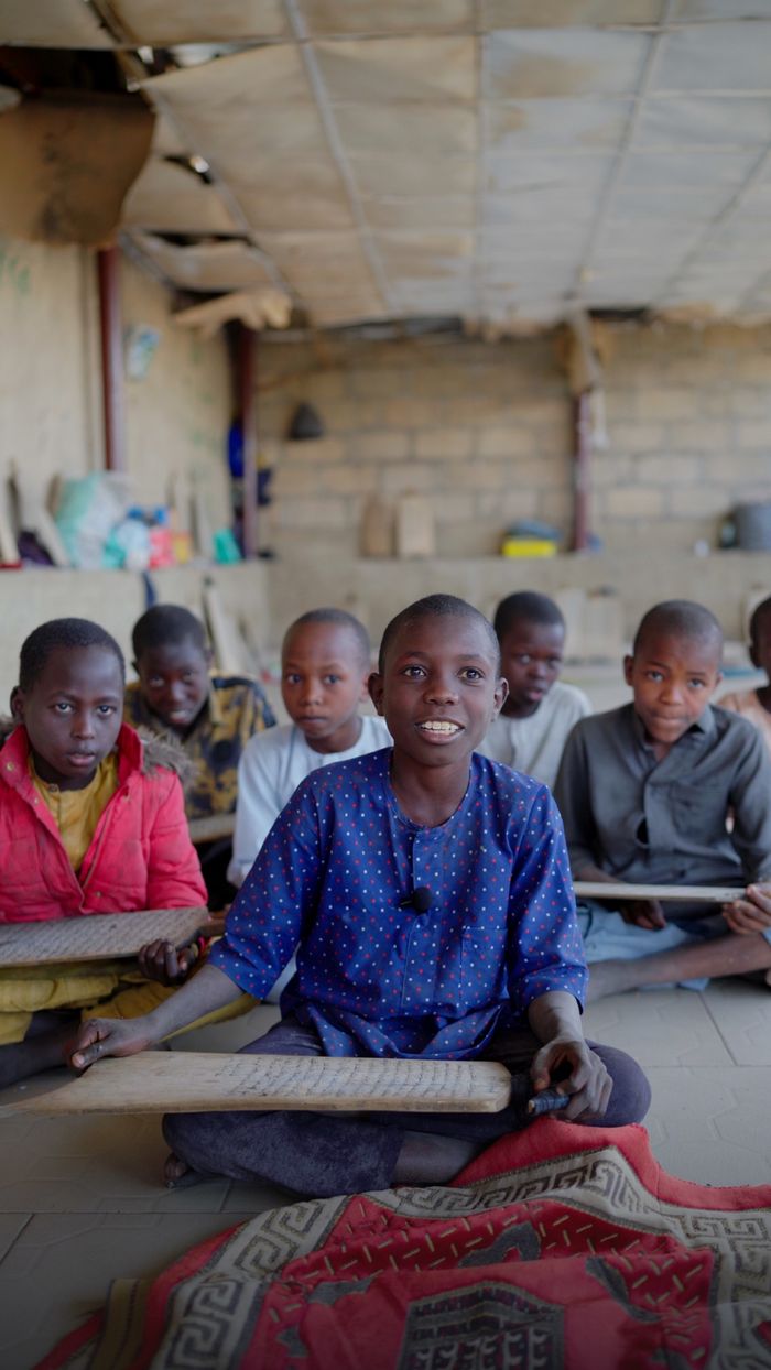 A group of smiling children engaged in a classroom activity, sitting on rugs indoors.
