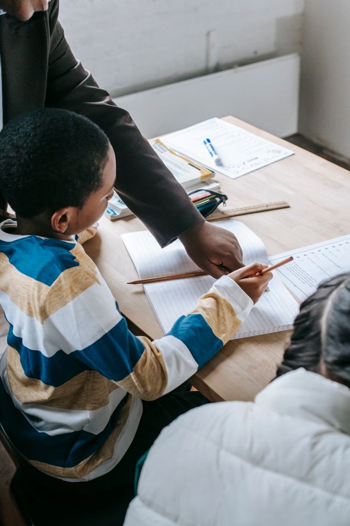 Crop black female helping ethnic boy and girl with assignment while studying in school classroom